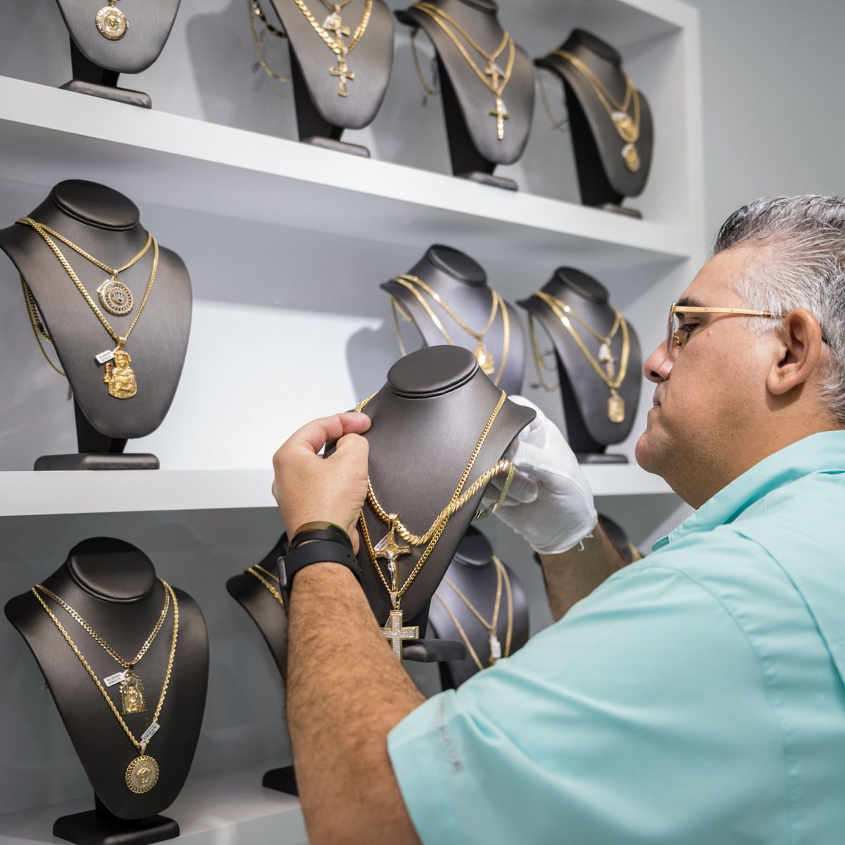 Misael wearing gloves, carefully placing a necklace on a mannequin.