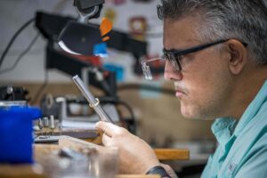 Misael carefully examines a ring while holding a ring resizing tool, focusing closely on the details.