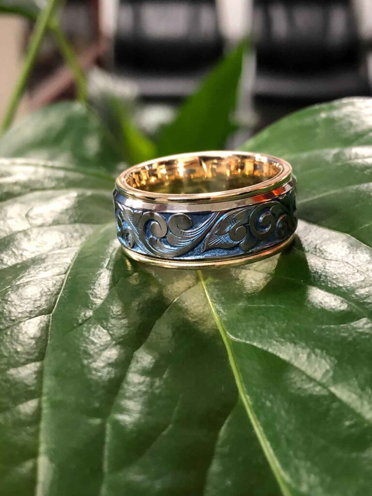 High-polish round gold ring resting on a green leaves, featuring a unique pattern on the band.