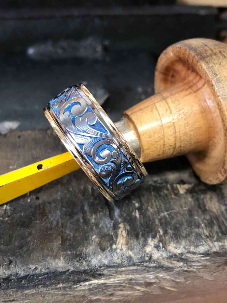 High-polish round gold ring on a palm engraving tool, featuring a unique pattern on the band.