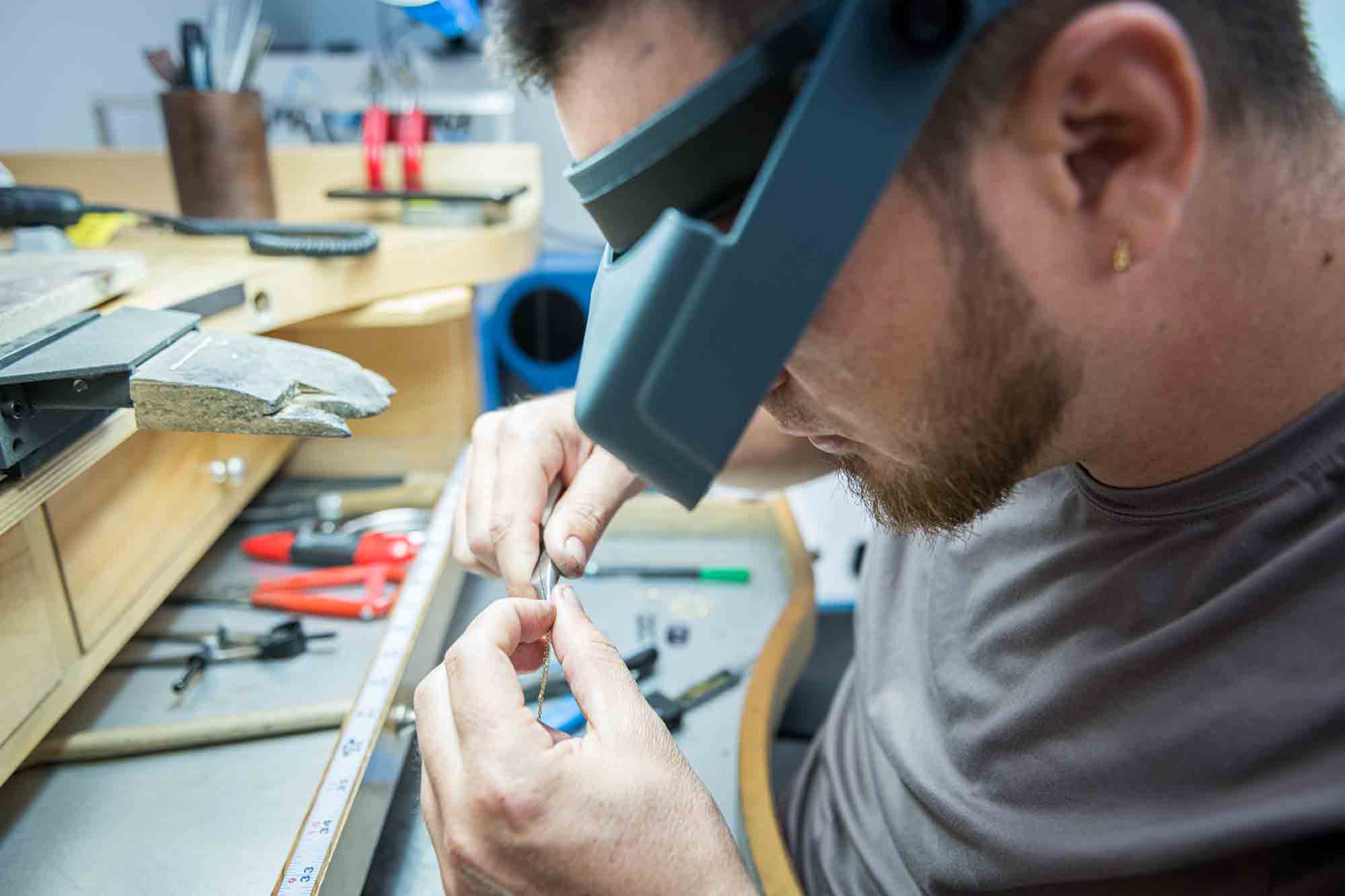 Jewelry technician with an headband magnifier while working on the thin chain holding a tweezer.