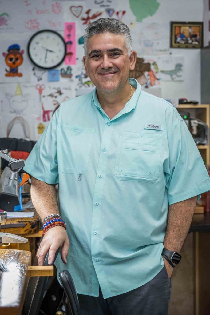 Owner - Misael on his blue-green blouse, standing and smiling.