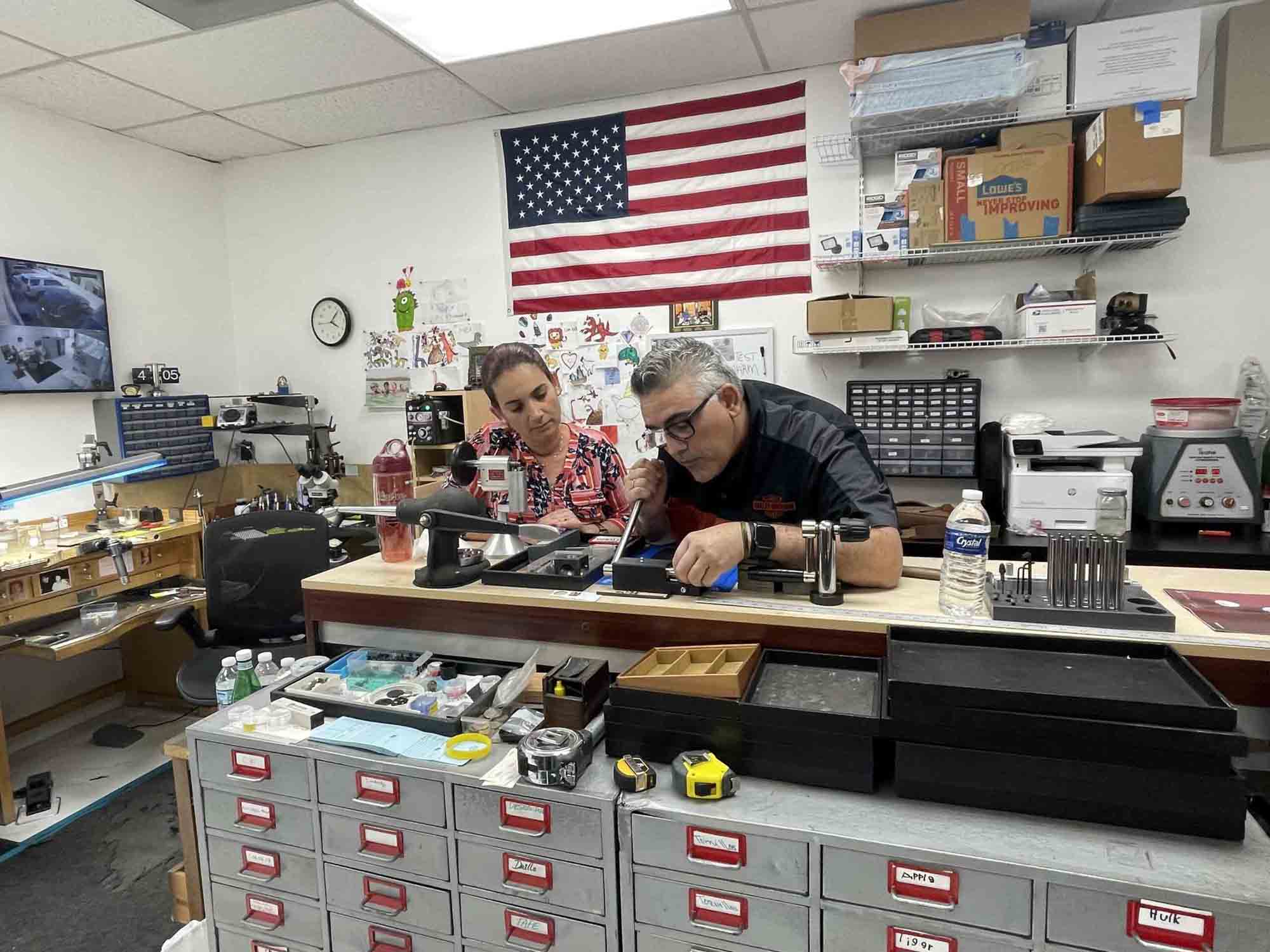 Misael is working with a tool while a woman stands beside him, observing his actions.