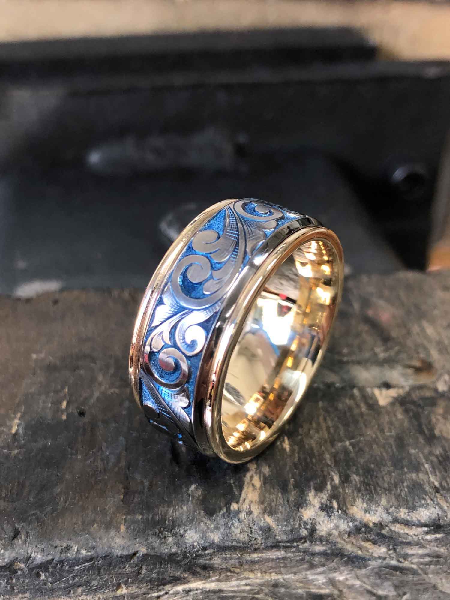 High-polish round gold ring placed upright on a wooden table, featuring an engraved, unique pattern on the band.