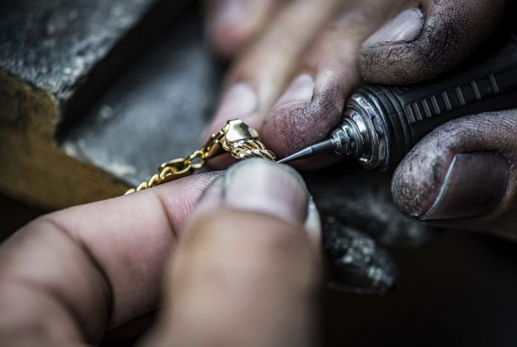 Jewelry technician holding a gold necklace pendant using a carving tool.