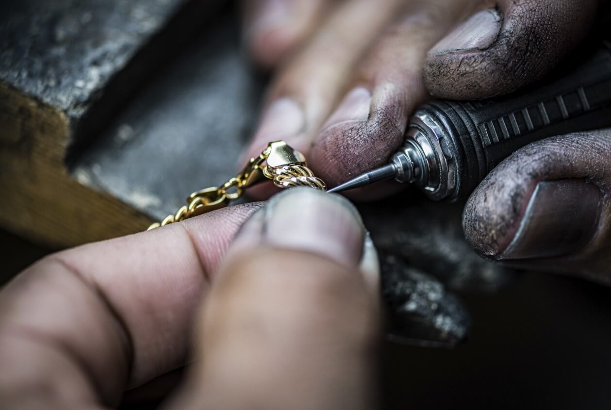 Jewelry technician holding a gold necklace pendant using a carving tool.