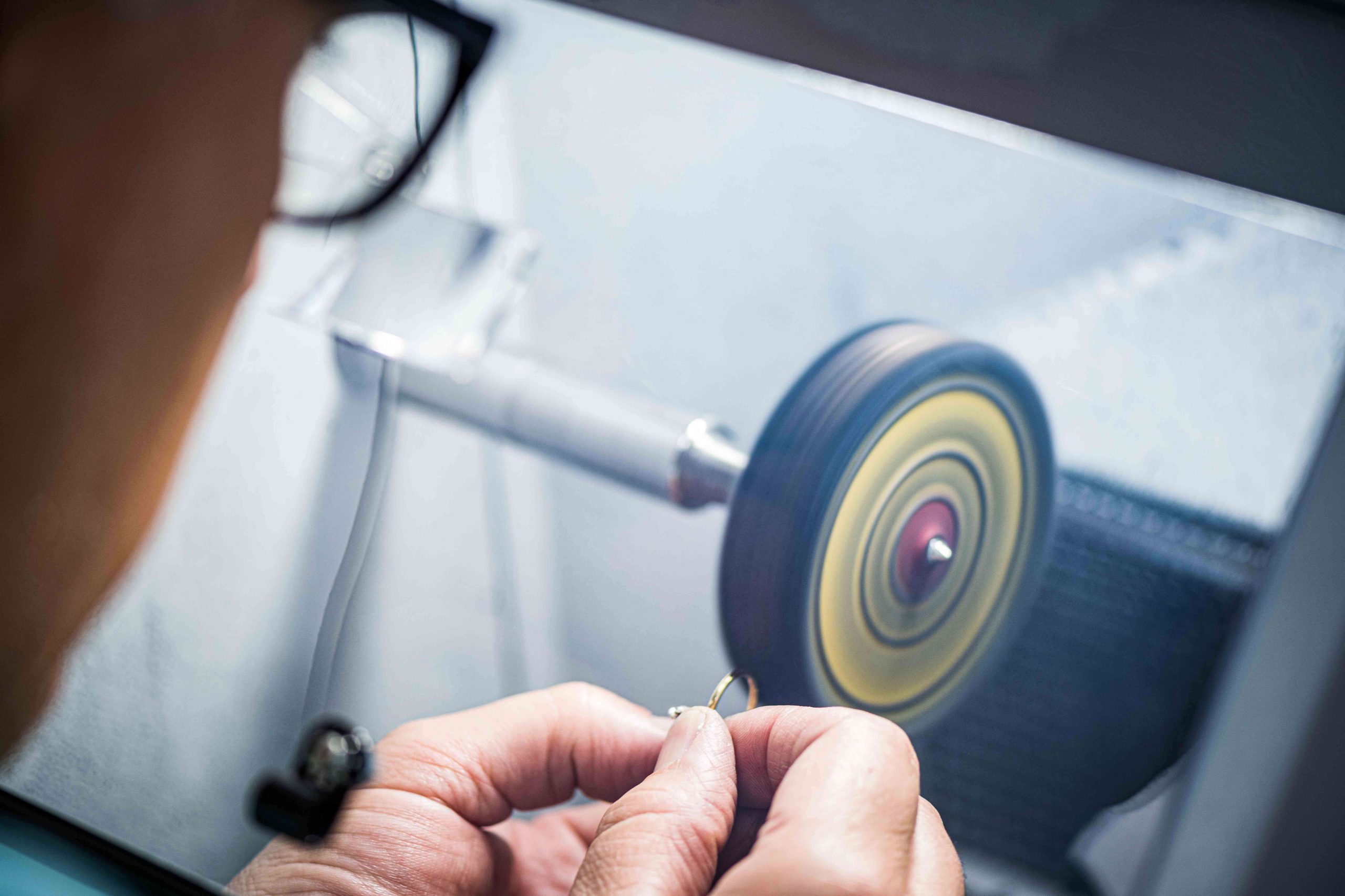 Jewelry technician holding a ring, directing it towards the polishing machine.